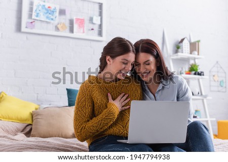 happy teenage girl and mother watching comedy movie on laptop in bedroom