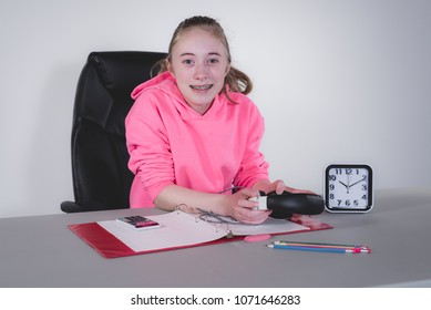 Happy teenage girl sitting at a desk studying/doing home work while holding headphones.