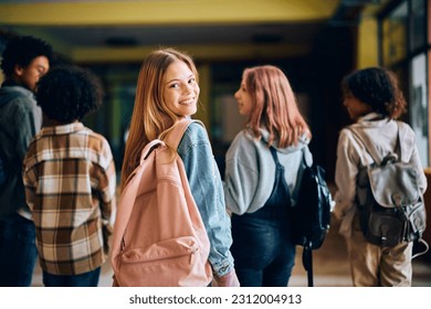 Happy teenage girl walking through high school hallway with her friends and looking at camera. 