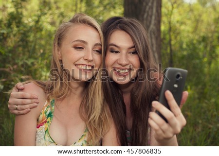 Happy teenage girls taking selfshot or selfy picture of themselves with mobile phone outdoors over green park