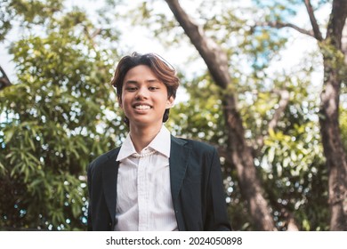 A happy teenage man of Filipino or Pacific Islander descent. In formal wear or university uniform posing outdoors.