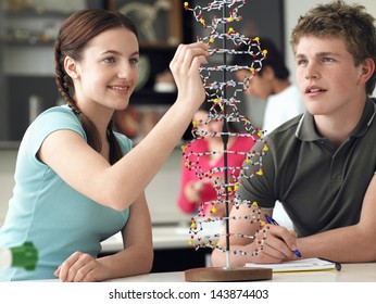 Happy Teenage Students Examining DNA Model And Taking Notes In Science Class