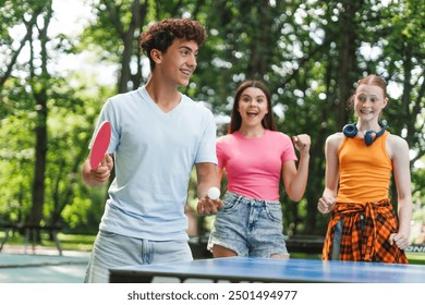 Happy teenager boy playing table tennis with racket and ping pong ball at park outdoors. Sport, lifestyle concept