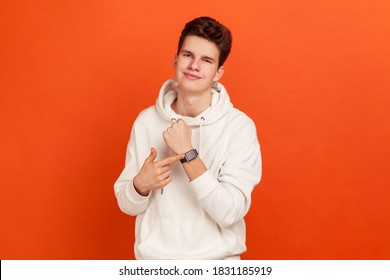 Happy teenager in casual style hoodie showing smartwatch on his wrist with smile on face, satisfied with gadget, contactless payments. Indoor studio shot isolated on orange background - Powered by Shutterstock