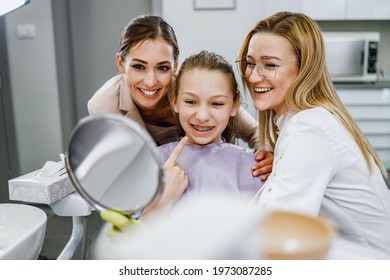 A Happy Teenager Girl Looking Her Teeth In A Mirror After Dental Procedure At Dentist's Office.