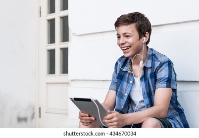 Happy teenager with a tablet sitting near the wall