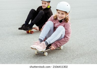 Happy Teenagers Boy And Girl Having Fun Skateboarding In Street In Helmets