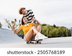 Happy teenagers boy girl school pupils classmates couple of students having fun skateboarding together in skate park ramp enjoy longboarding pushing friend on skateboard on road in urban street