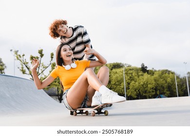 Happy teenagers boy girl school pupils classmates couple of students having fun skateboarding together in skate park ramp enjoy longboarding pushing friend on skateboard on road in urban street - Powered by Shutterstock