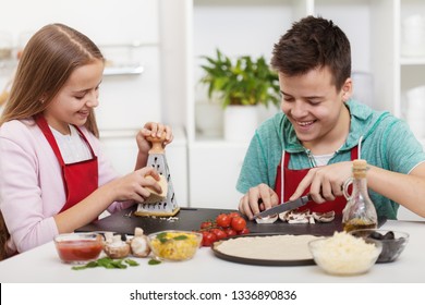 Happy teenagers having fun in the kitchen preparing a pizza and chatting with broad smiles on their faces