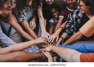 Happy teenagers putting their hands together in a huddle. Group of multicultural young kids stacking hands together in unity