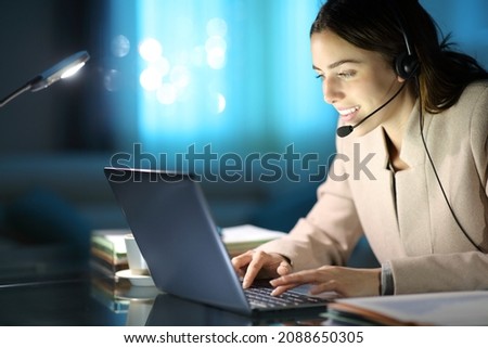 Happy tele marketer working with headset and laptop in the night at home