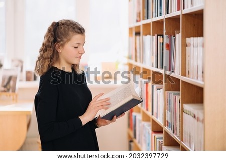 Happy tenage girl or student taking book from shelf in library - People, knowledge, education and school concept