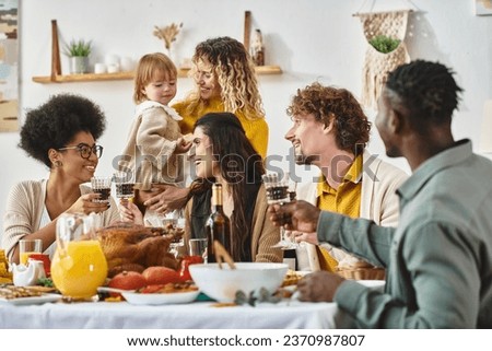 Happy Thanksgiving, cheerful multiethnic women clinking glasses of wine near friends and family
