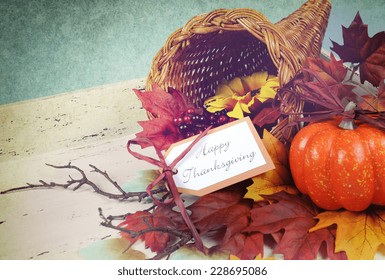 Happy Thanksgiving cornucopia with Autumn Fall leaves, pumpkin, sunflower and berries on white shabby chic tray against a pale blue background, with retro grunge filter.