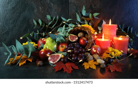 Happy Thanksgiving Cornucopia Table Setting Centerpiece Decorated With Autumn Leaves, Fruit, Nuts And Orange Burning Candles With Copy Space.