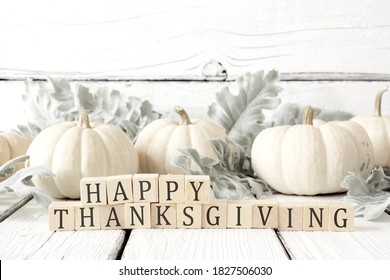 Happy Thanksgiving greeting on wooden blocks against a white wood background with white pumpkins and autumn leaves