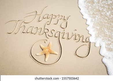 Happy Thanksgiving message handwritten on smooth sand beach with decorative starfish and oncoming wave - Shutterstock ID 1557503642