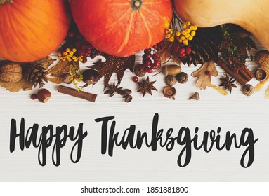 Happy Thanksgiving text sign on pumpkins, anise, cinnamon, acorn, nuts and autumn leaves on white wood flat lay. Seasons greetings. Happy Thanksgiving greeting card