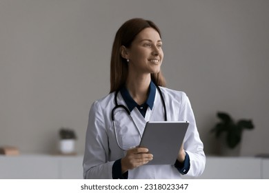 Happy thoughtful female doctor, physician using tablet computer at office, looking away, smiling, thinking. Medic professional using gadget for telemedicine, online consultation. Head shot portrait - Powered by Shutterstock