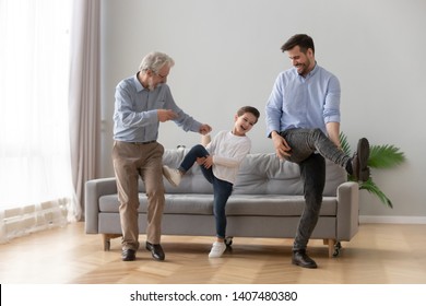 Happy Three Generations Of Men Have Fun Dancing Feel Overjoyed In Living Room, Smiling Millennial Father, Preschooler Son And Grandfather Entertain Relaxing At Home, Laugh Moving To Rhythm Together