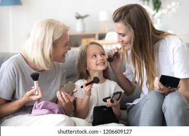 Happy three generations of women have fun at home laughing and doing make up for each other, smiling mother, daughter and grandmother enjoy time together, playing doing girly things