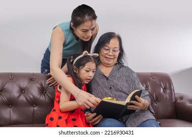 Happy Three Generations Of Women Reading Bible On Sofa.