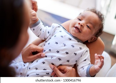 Happy three month old African American  baby boy lying on his back on his mothers knee looking up at her, over shoulder view, close up