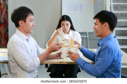 Happy Three Young Asian Colleague Friends Enjoy Eating Instant Noodles From Paper Cup With Chopsticks In Canteen Of Workplace Together. Friendship, Happiness, Fast Food Lunch And Lifestyle Concept