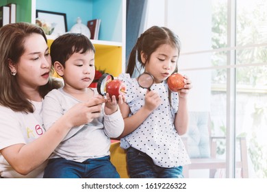 Happy Time Of Family. Mom Teach Her Son And Daugher To Used Magnifying Glass Looking On Apple At Home. Learning And Discovery Concept.