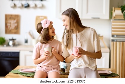 Happy time with mom. Young lovely mother and cute little daughter drinking tea and smiling while standing together in modern cozy kitchen, older and younger sister enjoying family weekend at home - Shutterstock ID 2124313376