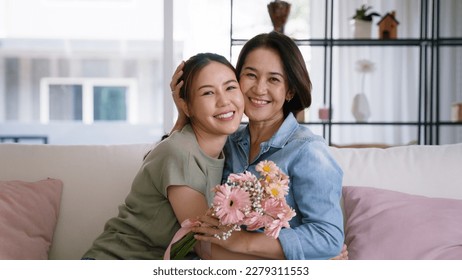 Happy time Mother day grown up child girl looking at camera cuddle hug give flower bouquet gift to mature mum. Love kiss care mom asia middle age adult people smile enjoy relax sitting at home sofa. - Powered by Shutterstock