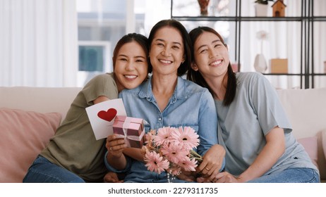 Happy time Mother day grown up child looking at camera cuddle hug give flower gift box red heart card to mature mum. Love kiss care mom asia middle age adult people smile enjoy sitting at home sofa. - Powered by Shutterstock