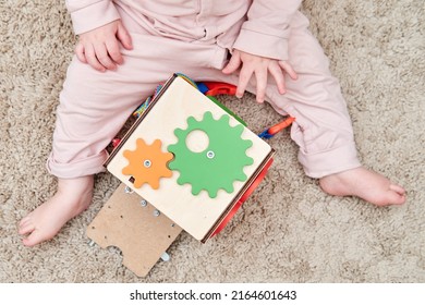 Happy Toddler Baby Boy Is Playing With A Busyboard Cube On The Nursery Floor. Educational Toys For Children, Wooden Game Panel. A Child Aged One Year