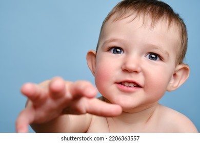 Happy Toddler Baby Boy Reaching Out With His Hand, Studio Blue Background. Portrait Of A Smiling Cute Child, Close-up. Kid Aged One Year And Two Months