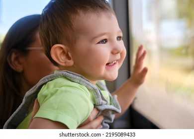 A Happy Toddler Boy Looks Out The Bus Window While Sitting In The Arms Of His Mother. Child In Transport With A Parent, Close-up