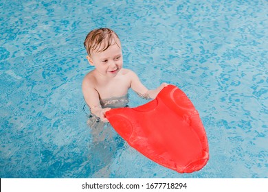 Happy Toddler Boy Swimming With Flutter Board In Swimming Pool