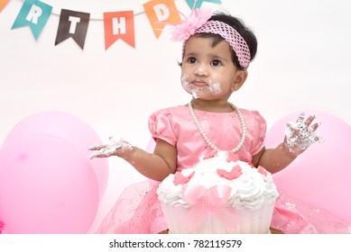 Happy toddler eating birthday cake; cake smash photosession, Indian baby girl smash cake