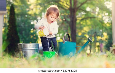 Happy Toddler Girl Playing With Watering Cans Outside 