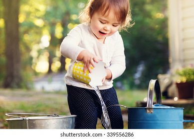 Happy Toddler Girl Playing With Watering Cans Outside