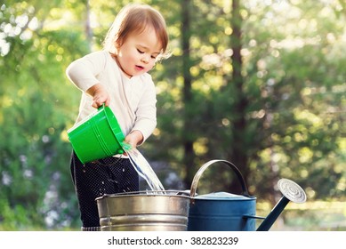 Happy Toddler Girl Playing With Watering Cans Outside