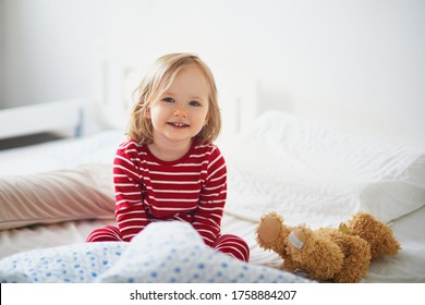 Happy Toddler Girl In Striped Red And White Pajamas Sitting On Bed Right After Awaking. Day Naps For Small Kids