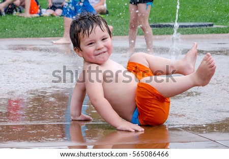 A happy toddler shows off as he plays in a urban splash pad