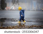 Happy toddler walks through the puddles in blue jumpsuit with splashes close-up and copy space.