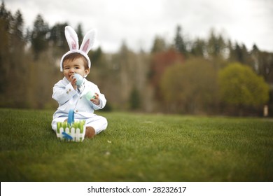 Happy toddler wearing rabbit ears trying to eat the plastic egg at the park.