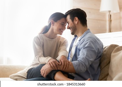 Happy together. Smiling newlyweds cuddling on couch at living room of rented purchased flat, caring husband hugging holding on knees beloved wife, young couple is glad to start new independent life - Shutterstock ID 1845313660