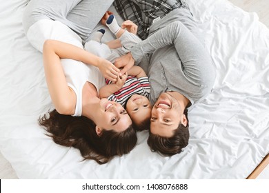 Happy Together. Young Family With Baby Lying In Bed, Top View, Upside Down Photo