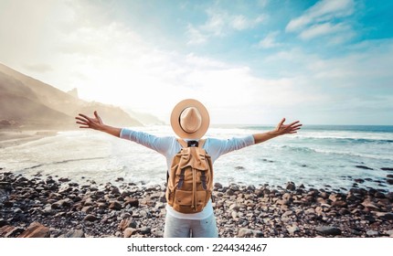 Happy tourist with backpack enjoying freedom raising arms up - Wellbeing, journey and tourism concept - Shutterstock ID 2244342467