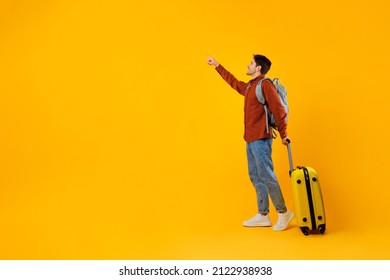 Happy Tourist Man Pointing Finger Aside Standing With Travel Suitcase And Backpack Posing Over Yellow Studio Background. Tourism And Vacation Offer Concept. Full Length, Empty Space For Text