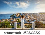 A happy tourist woman enjoys the beautiful summer sunset view of the town of Skiathos island, Sporades, Greece